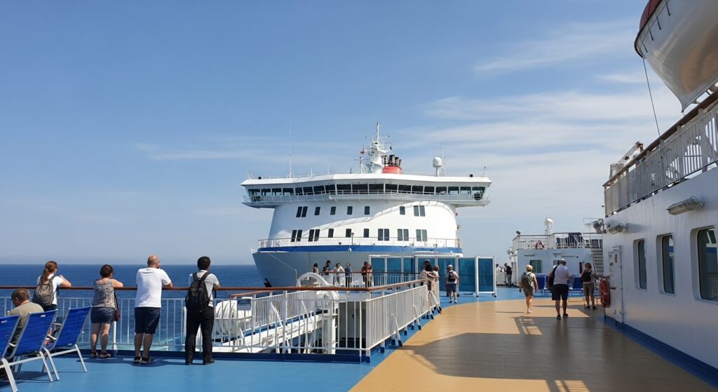 フェリーの展望デッキで海を眺めながら過ごす乗客たち。船内で自由にリラックスできる様子が伝わる風景。