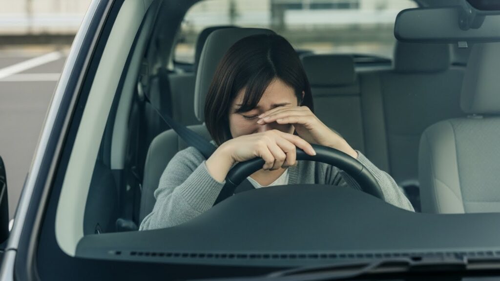 運転に不安を感じ、車内でハンドルを前に立ちすくむ女性の様子